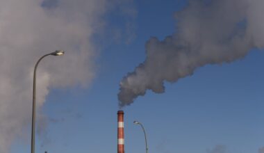 A red-and-white striped smokestack emits a grey cloud a smoke into the air wintry air.