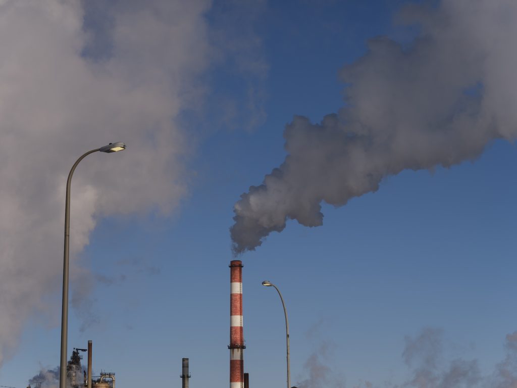 A red-and-white striped smokestack emits a grey cloud a smoke into the air wintry air.