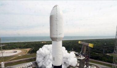 a close-up of a payload fairing atop a rocket as it lifs off from its ocean-side launch pad