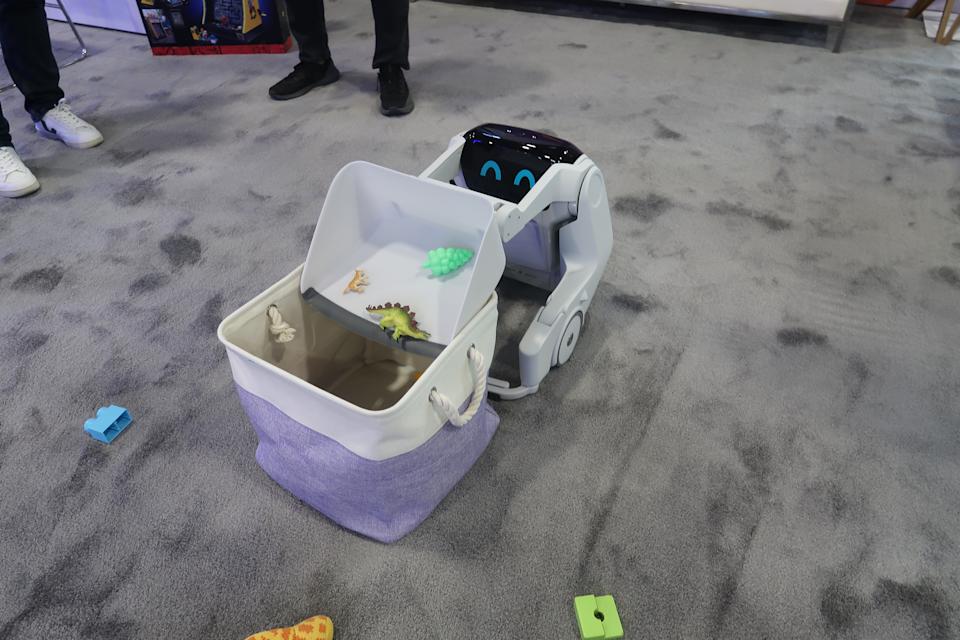A robot with a dust pan like appendage dumps toys into a bin