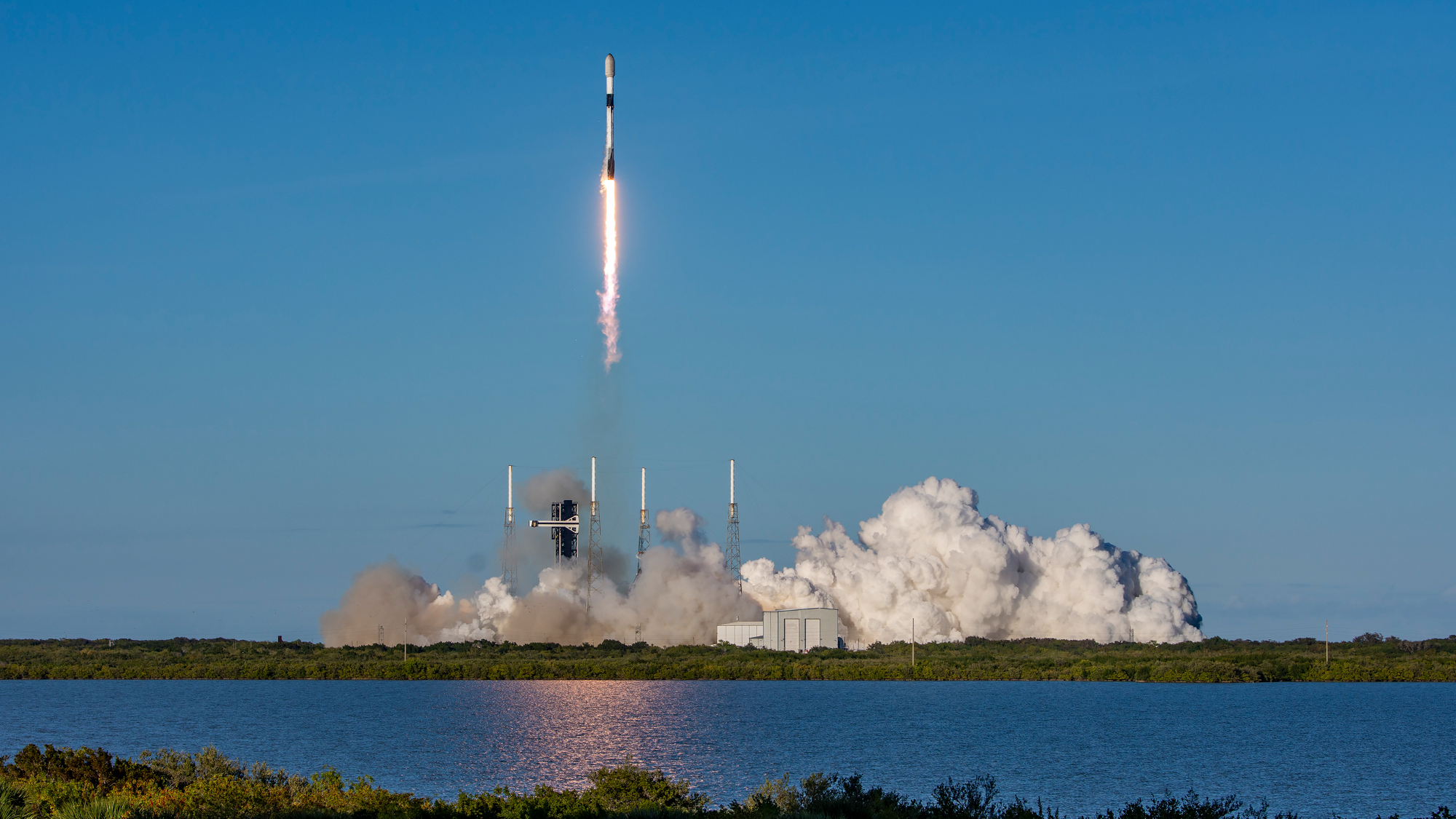 a black-and-white spacex falcon 9 rocket launches into a blue sky.