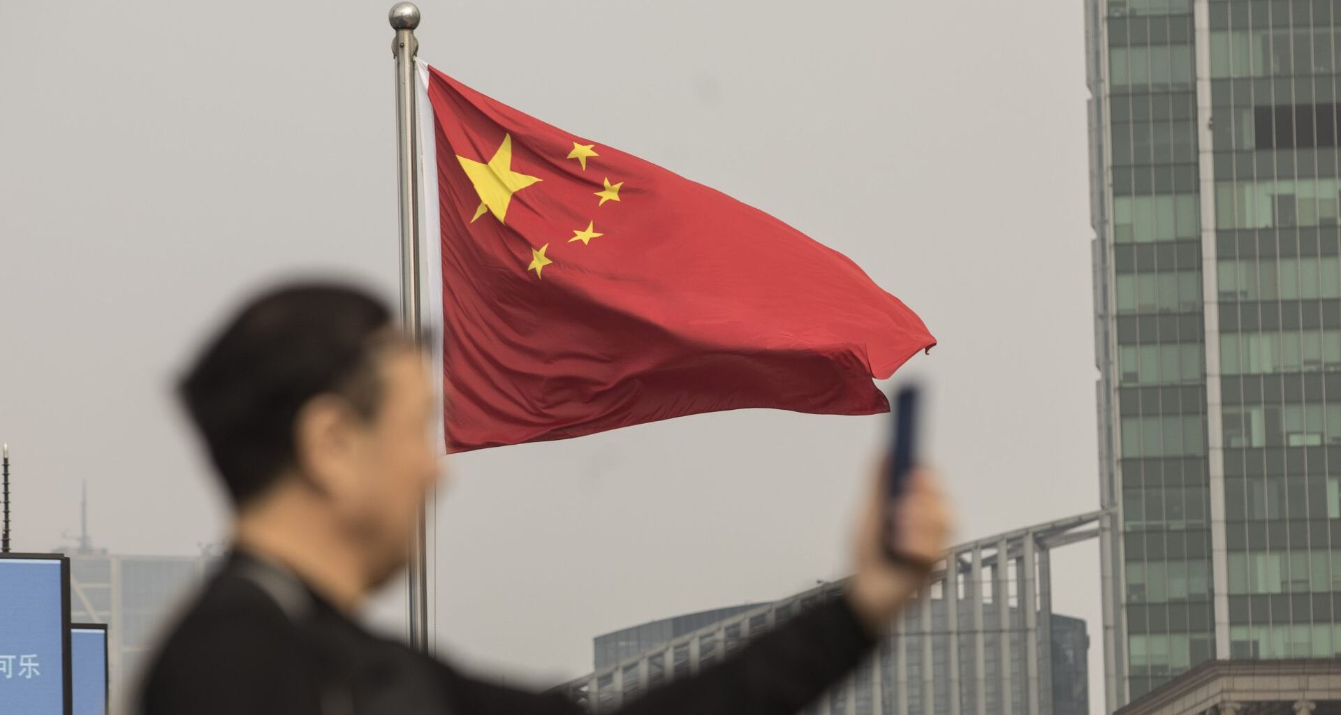 Man looking at phone on backdrop of Chinese flag