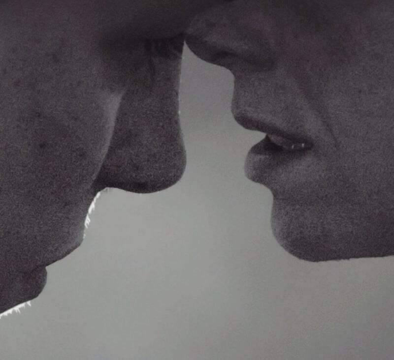 A close-up, grayscale image of two people's faces, nearly touching, with focus on their noses and lips. The mood appears intimate and emotional.
