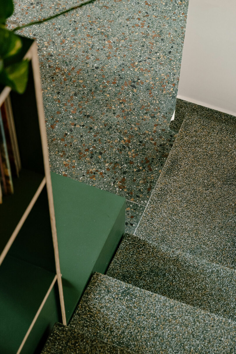 A close-up view of stairs with a speckled green and brown terrazzo surface, next to a green bookcase and a white wall.
