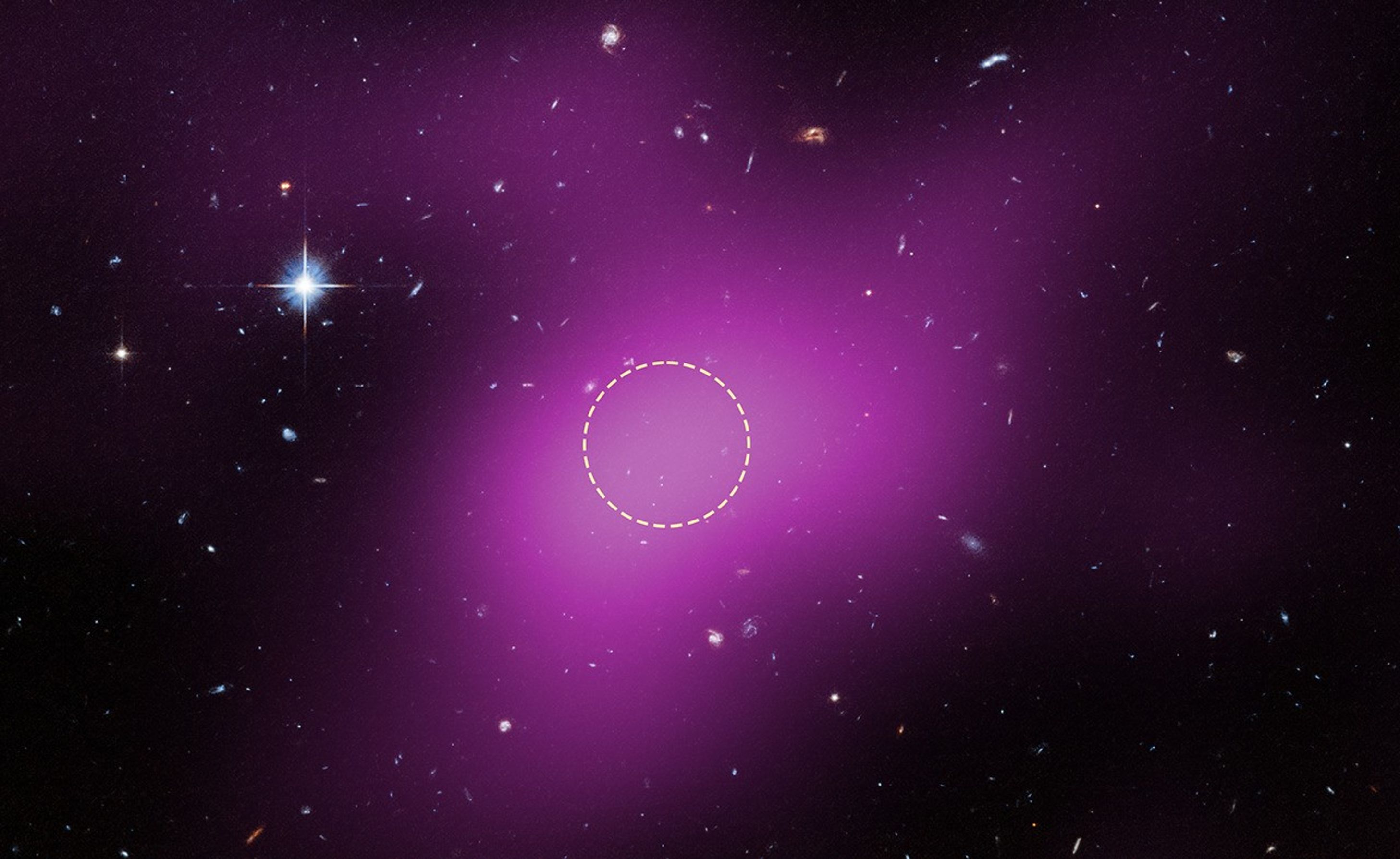A region of space mostly filled with background galaxies, with one prominent star at upper left. A large blob of purple haze occupies much of the field. Within the purple region, an unremarkable area is outlined with a dashed white circle.