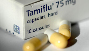A box of Tamiflu with yellow and white capsules sitting outside of it.