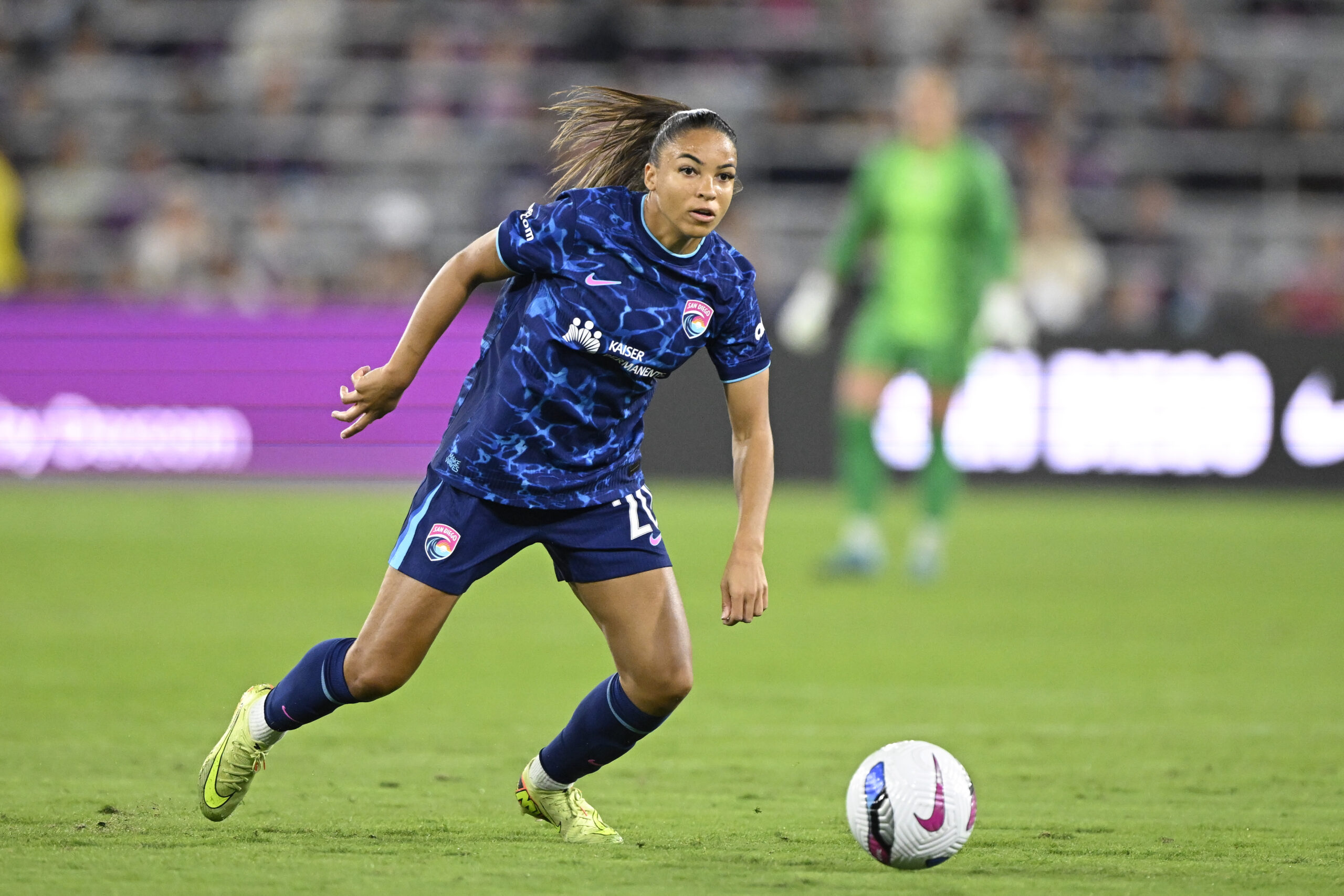 A soccer player in a blue uniform controls the ball on the field