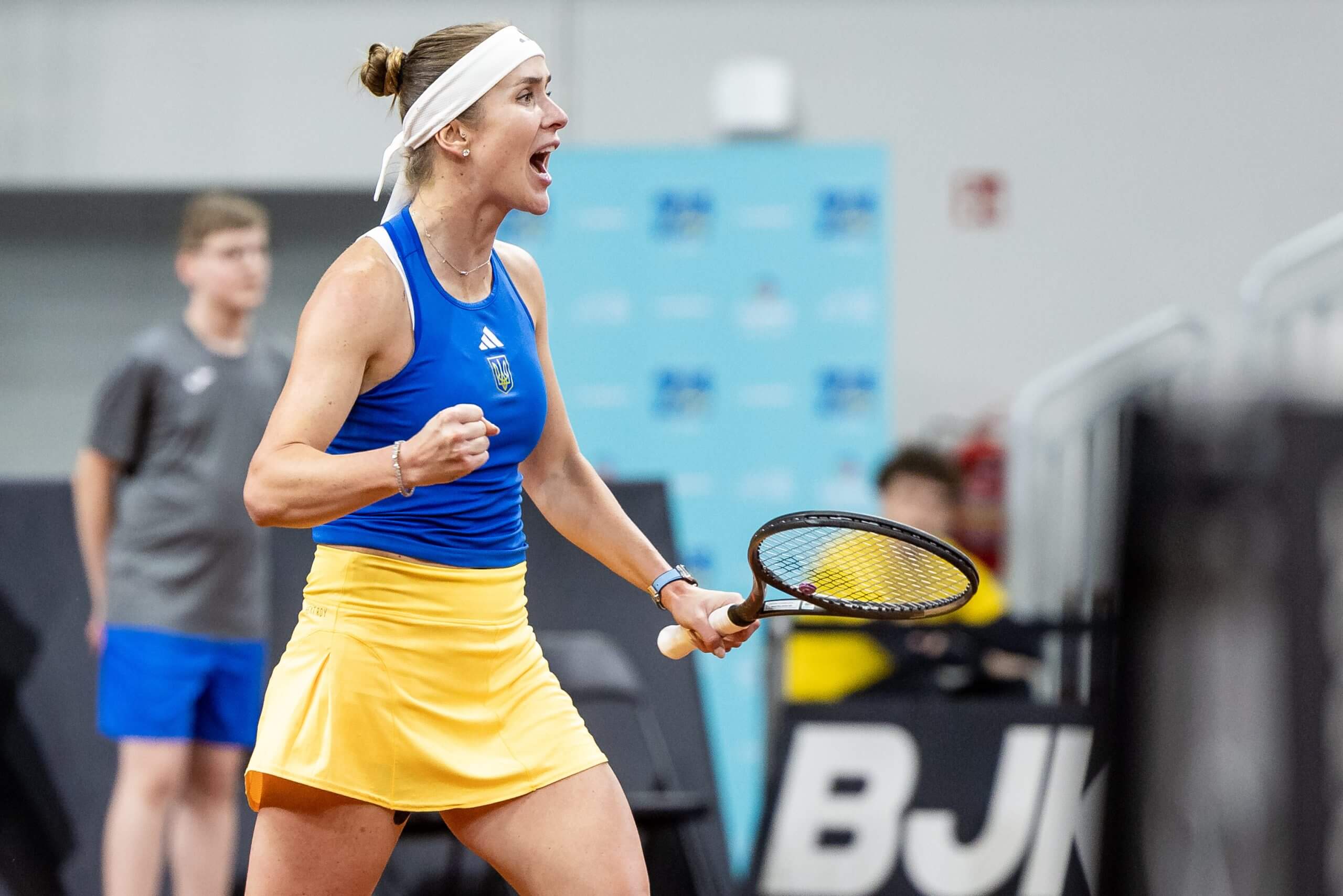 Elina Svitolina celebrates on a tennis court wearing Ukraine's colors.