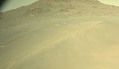 A greenish tinted image with a large hill in the distance and smaller sandy dunes in front