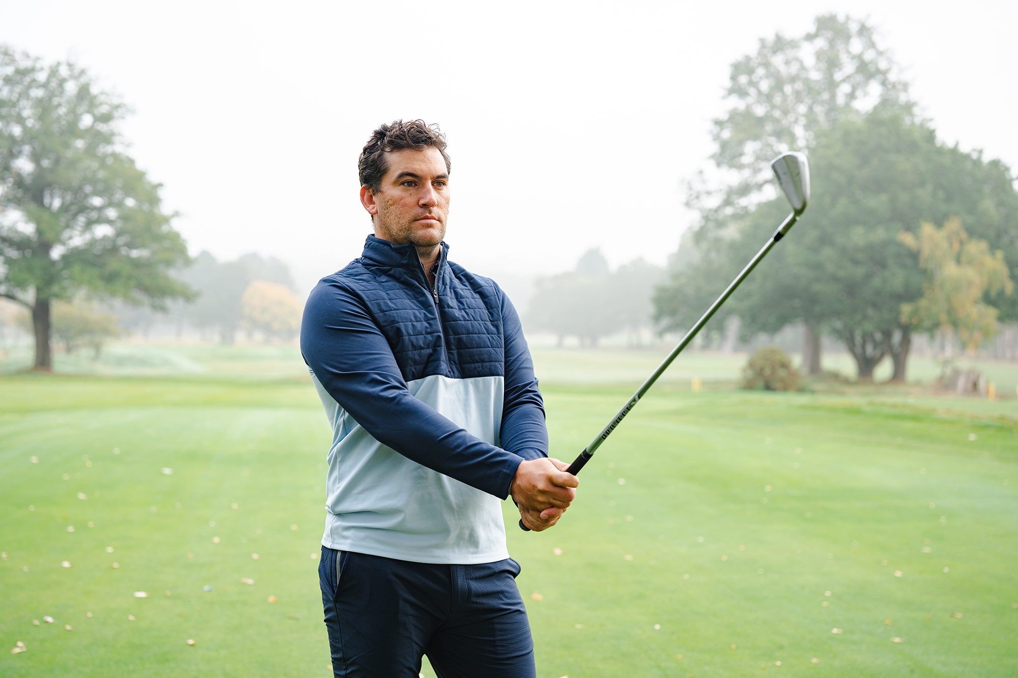 Sam De'Ath lining up a golf shot with his club outstretched in front of him on a wintery day on the golf course