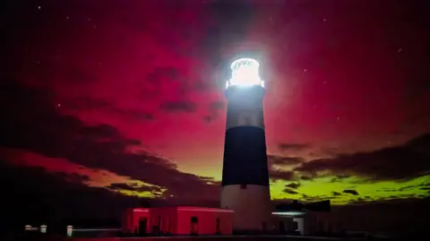 STEVIE PHE Light house with Northern lights in the backgrond, they are red and yellowy green