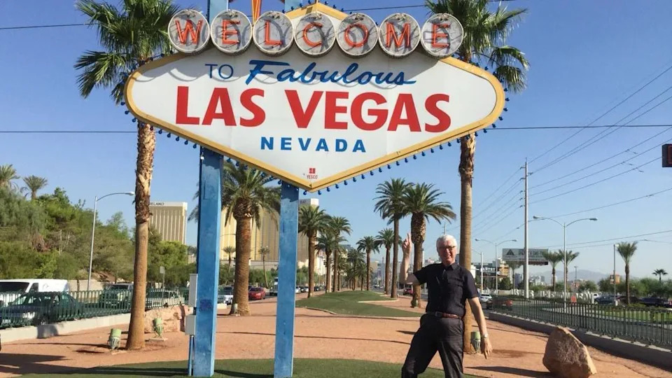 Nigel Thomas is pictured a few years ago on holiday in Las Vegas. He is standing beneath one of the famous road signs that welcomes visitors to Las Vegas. It is large, lozenge-shaped, and has red and blue writing on a white background saying 'welcome to fabulous Vegas Nevada'.