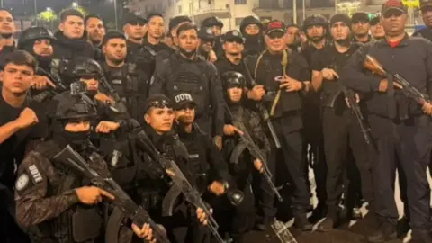 Instagram/@Minsjustice_VE Interior Minister Diosdado Cabello poses with a group of uniformed men, some of whom are holding machine guns, with others wearing helmets and/or body armour.