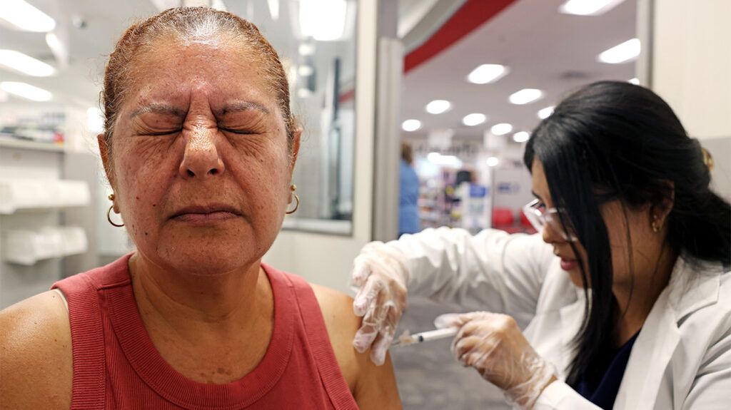 older woman tightly shutting her eyes while getting vaccinated