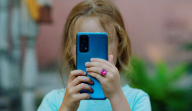 A child holds a cell phone, obscuring her face.