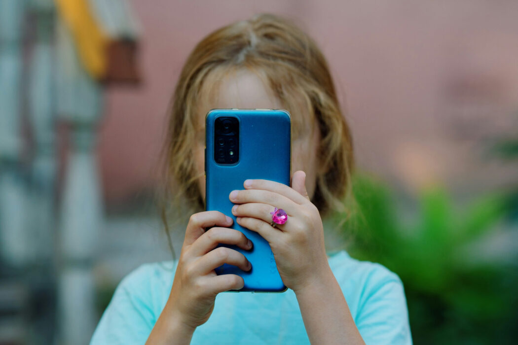 A child holds a cell phone, obscuring her face.