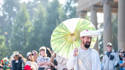Heidi Alletzhauser/California Academy of Sciences Press Office A person wearing a white alligator hat and holding a lime green umbrella in front of a crowd