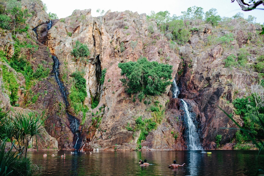 Bathers swim at the base of a large rock waterfall