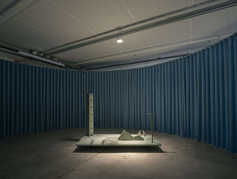 a circular enclosure formed by blue curtains defines an intimate room within the larger infrastructural hall