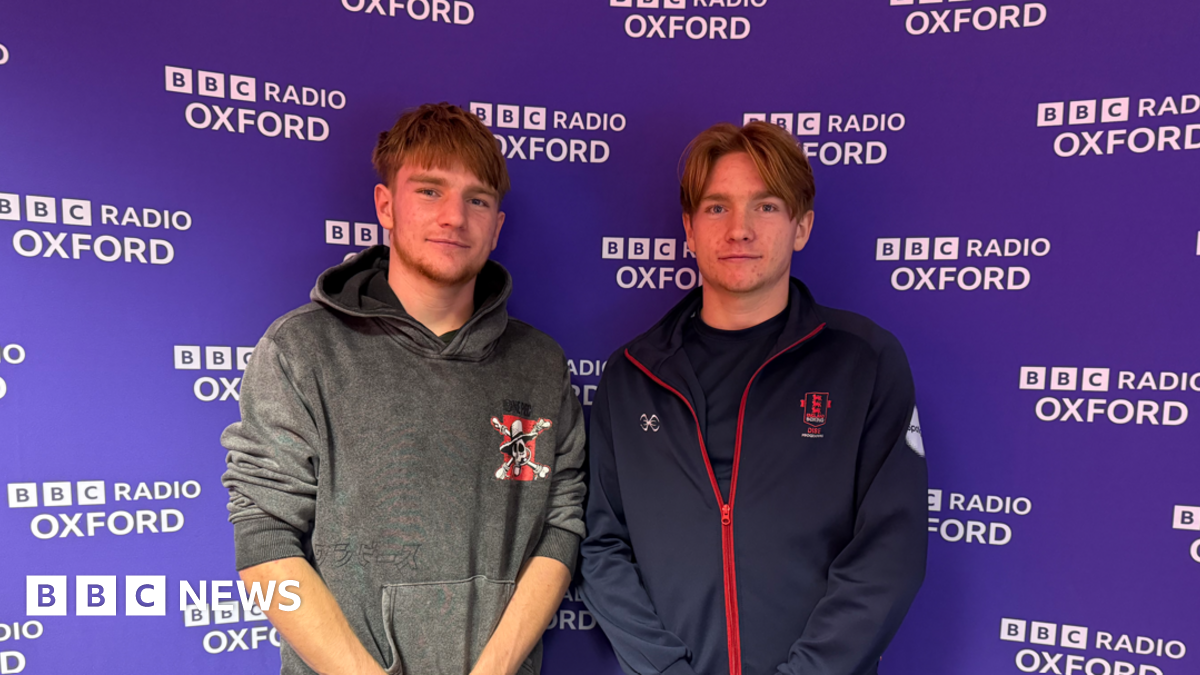 Identical twins Chris and Johnny standing in front of a purple BBC branded background.