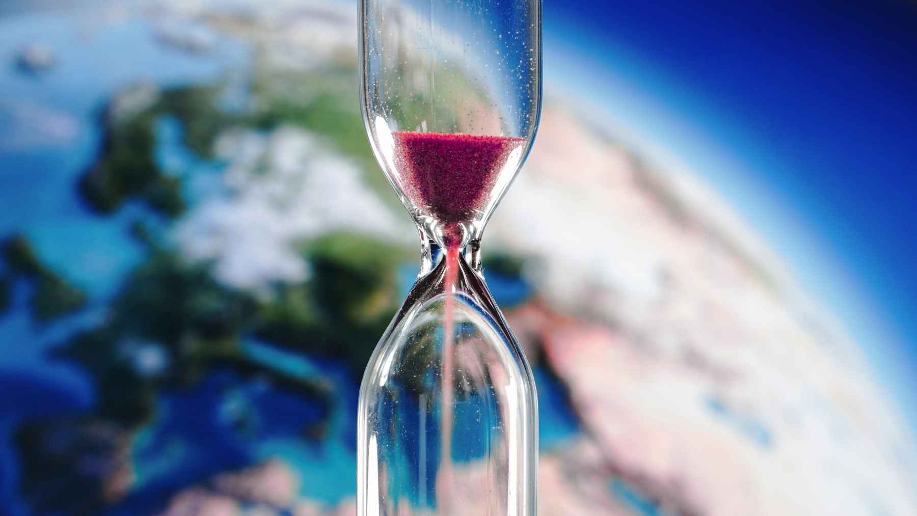 An hourglass floating in front of Earth, symbolizing how climate change is affecting the planet’s rotation and global timekeeping.