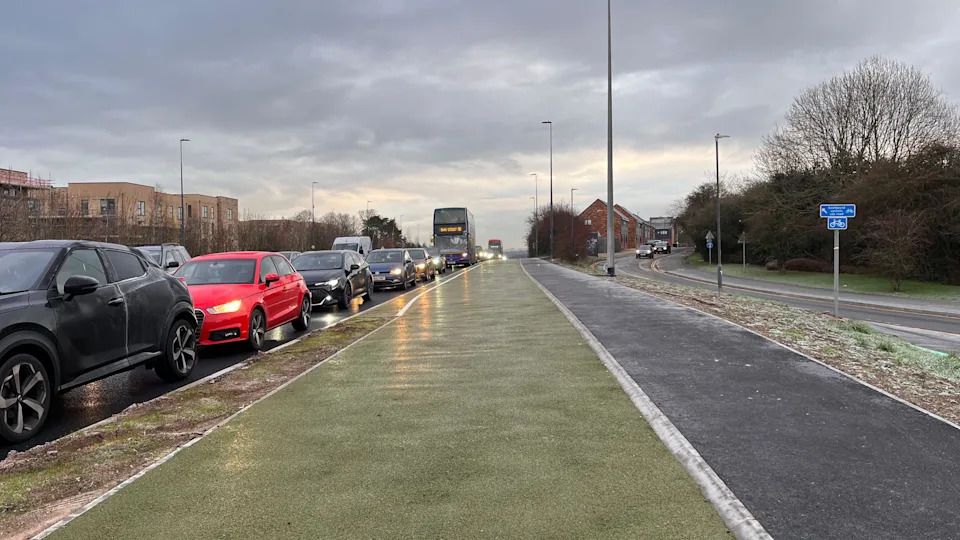A green cycle lane next to a grey cycle path, pictured facing the incoming traffic, in a grey icy morning.