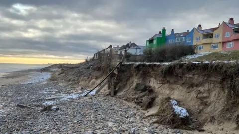 Richard Daniel/BBC An image taken on a beach showing the sea and a row of rainbow-coloured houses perched close to a cliff edge in Thorpeness.