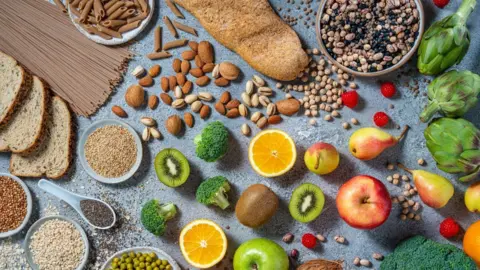 Getty Images A range of food spread across a table, including kiwis, broccoli, apples, seeds, nuts, bread, brown pasta
