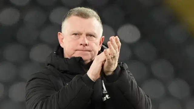 Mark Robins claps his hands towards fans