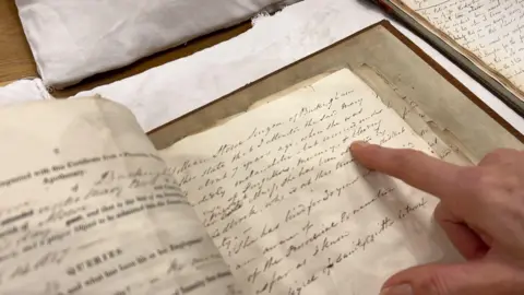 A woman's finger pointing at an archive record.