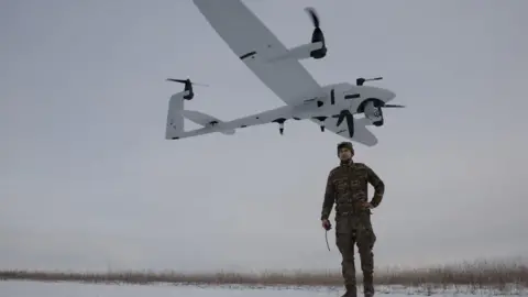 Reuters A Ukrainian serviceman in camouflage uniform stands on snow-covered ground after launching a reconnaissance unmanned aerial vehicle seen above his head