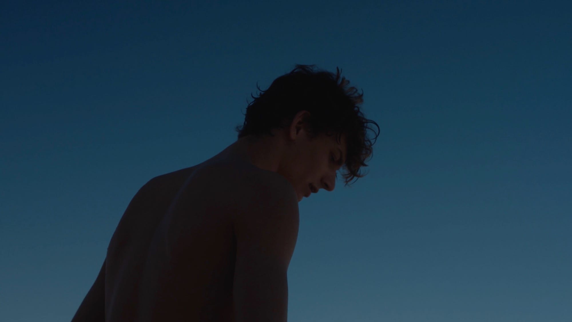A still from a short film of a young man silhouetted against a dark blue sky