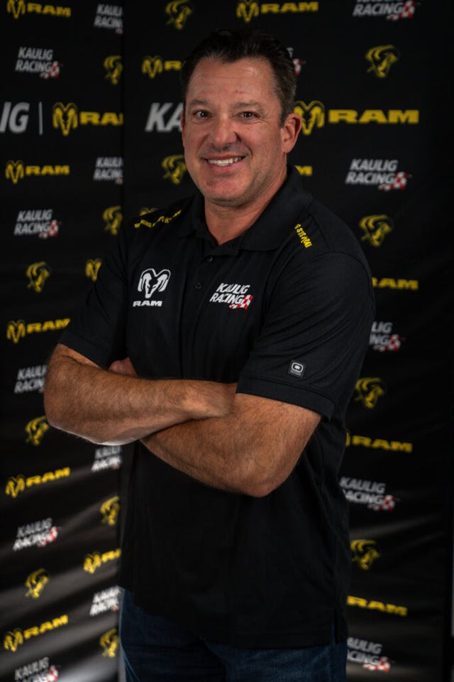 person in a black polo shirt featuring automotive branding with arms crossed