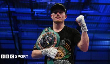 Dalton Smith poses in a dark baseball cap after a win, with a raised left fist and a title belt over his right shoulder