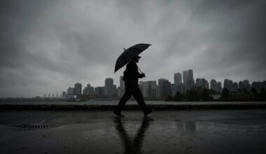 A man uses an umbrella to shield himself from the rain while walking on the Stanley Park seawall across the water from downtown Vancouver, B.C., Oct. 19, 2024. THE CANADIAN PRESS/Darryl Dyck