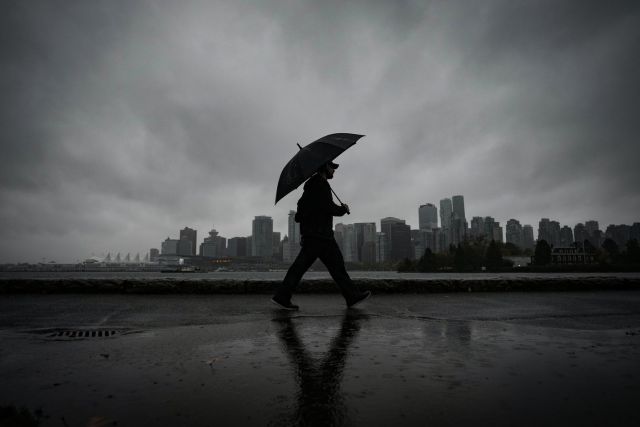 A man uses an umbrella to shield himself from the rain while walking on the Stanley Park seawall across the water from downtown Vancouver, B.C., Oct. 19, 2024. THE CANADIAN PRESS/Darryl Dyck