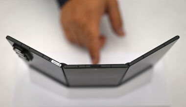 A person points their finger at at a phone with three screens propped up.