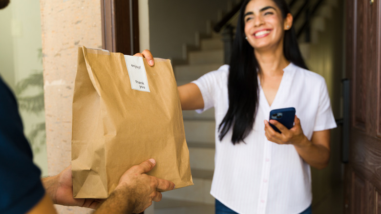 A woman accepting food delivery in a brown bag