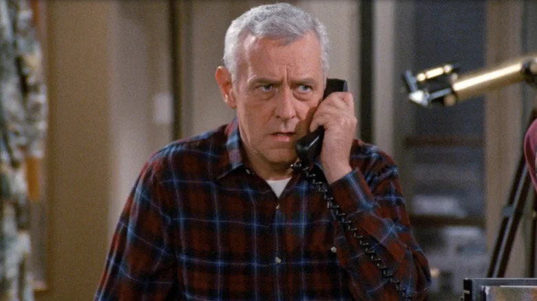 John Mahoney as Martin in red plaid shirt looking concerned with telephone to his ear in Frasier
