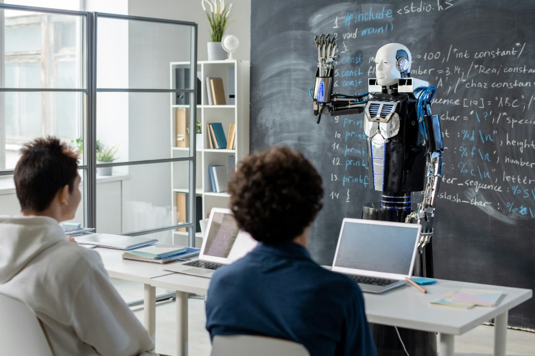 A humanoid robot figure stands in a classroom, in front of a blackboard, with one arm raised stiffly. Two students look on.