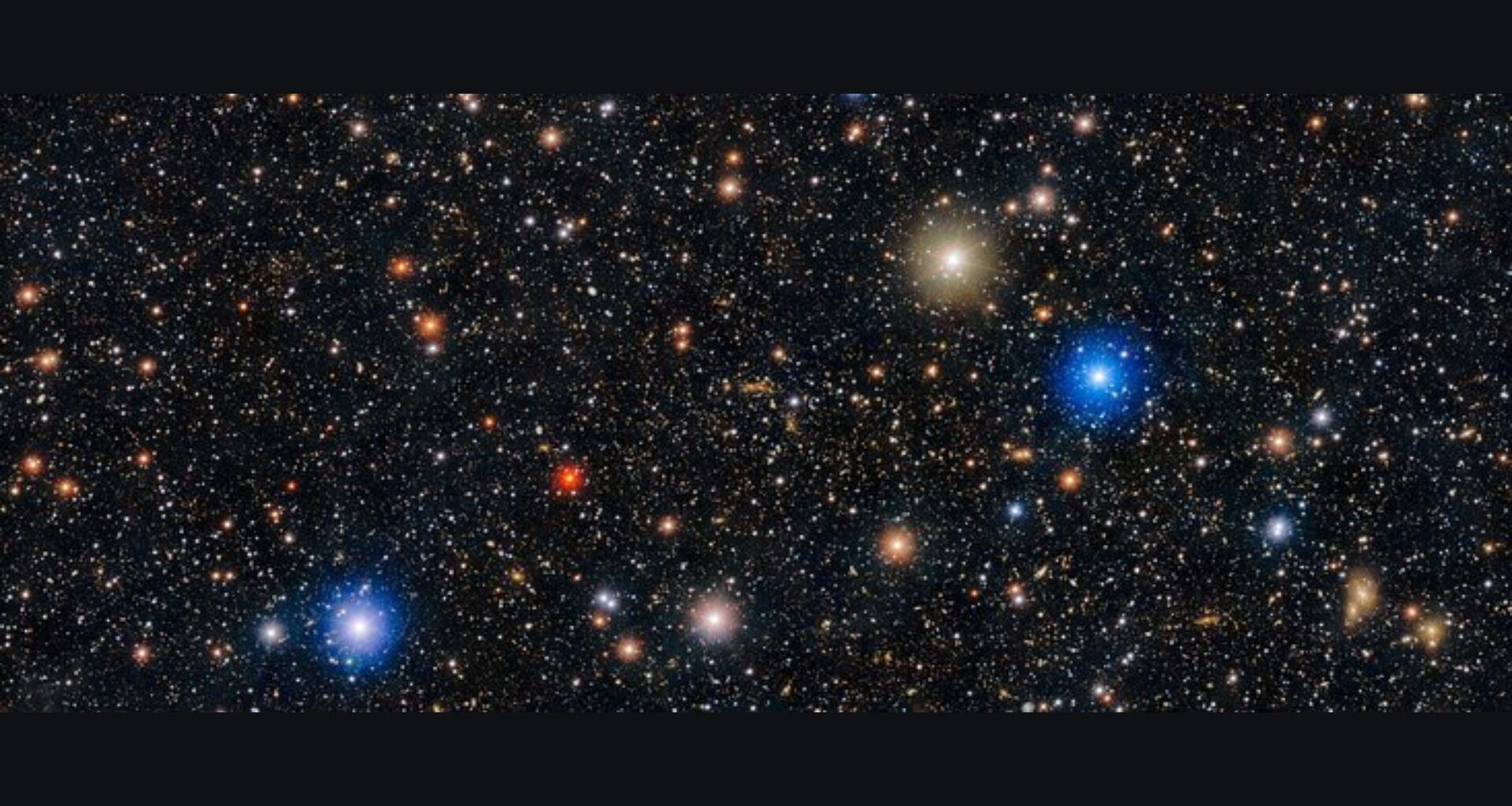 Image of space showing a black sky with hundreds of white dots and a few red, orange, gold and blue dots with halos of light surrounding them.
