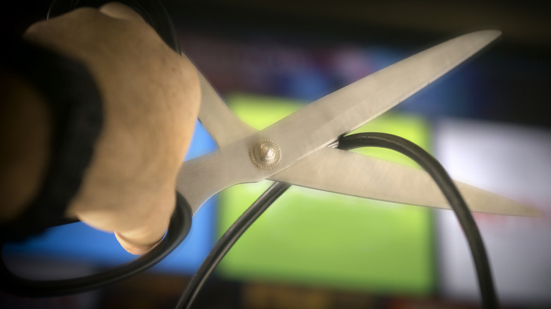 Hand holding scissors that are cutting a cord