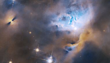 Within a ghostly blue and orange cloud of gas and dust, several stars shine brightly. To the upper left is a protoplanetary disk, appearing as a bright point flanked on either side by fan-shaped shadows. To the center right, stars are nestled in a cavity in the gas and dust.