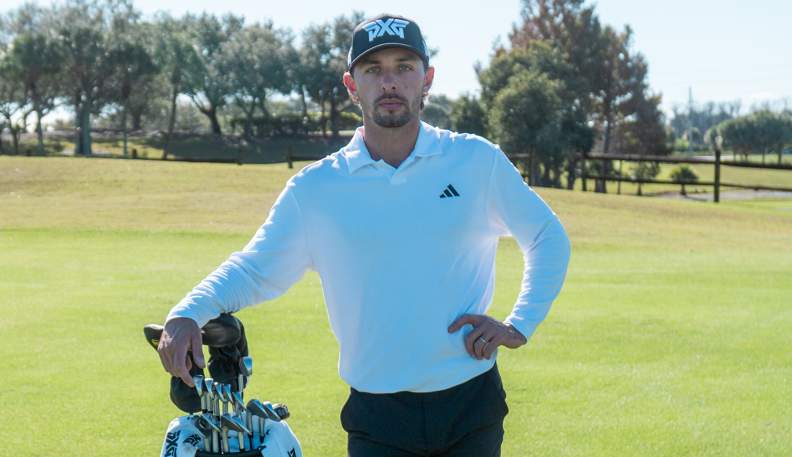Marco Penge poses next to a golf bag wearing PXG and adidas clothing