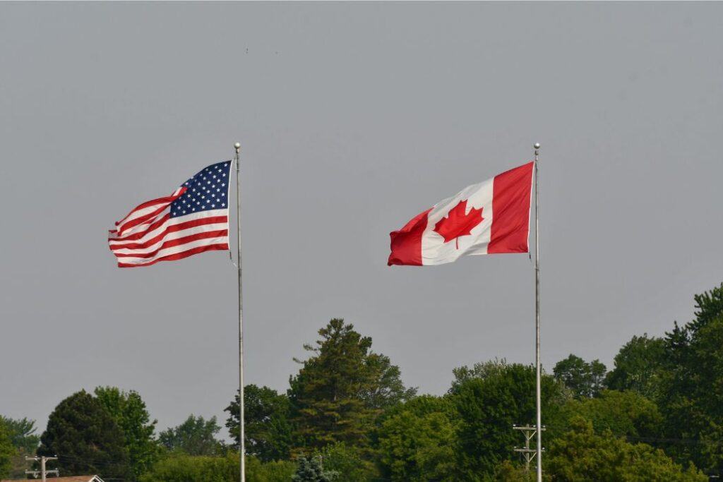 A Canadian and American flag flap int eh wind, side by side.