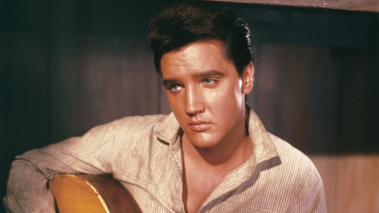 Young Elvis Presley sat looking sullen holding guitar