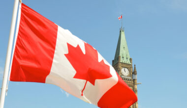 Canadian flag flies in the foreground over the parliament buildings in Ottawa on a sunny day