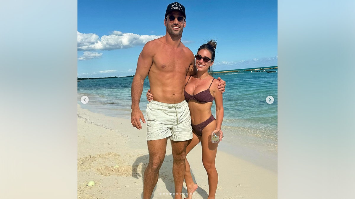 Jessie James Decker and her husband standing on the beach in their swimsuits.