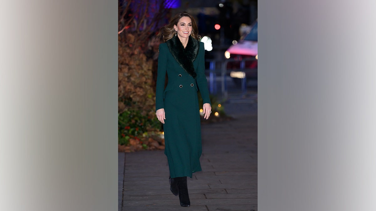 Kate Middleton walks outdoors in London wearing a green coat dress with a black fur collar during a December 2025 appearance.