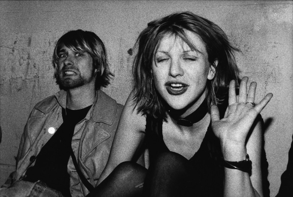 Kurt Cobain grimacing next to Courtney Love who is waving